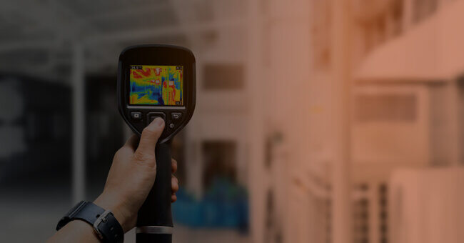 A person holds a thermal imaging camera inside a laboratory or industrial workspace